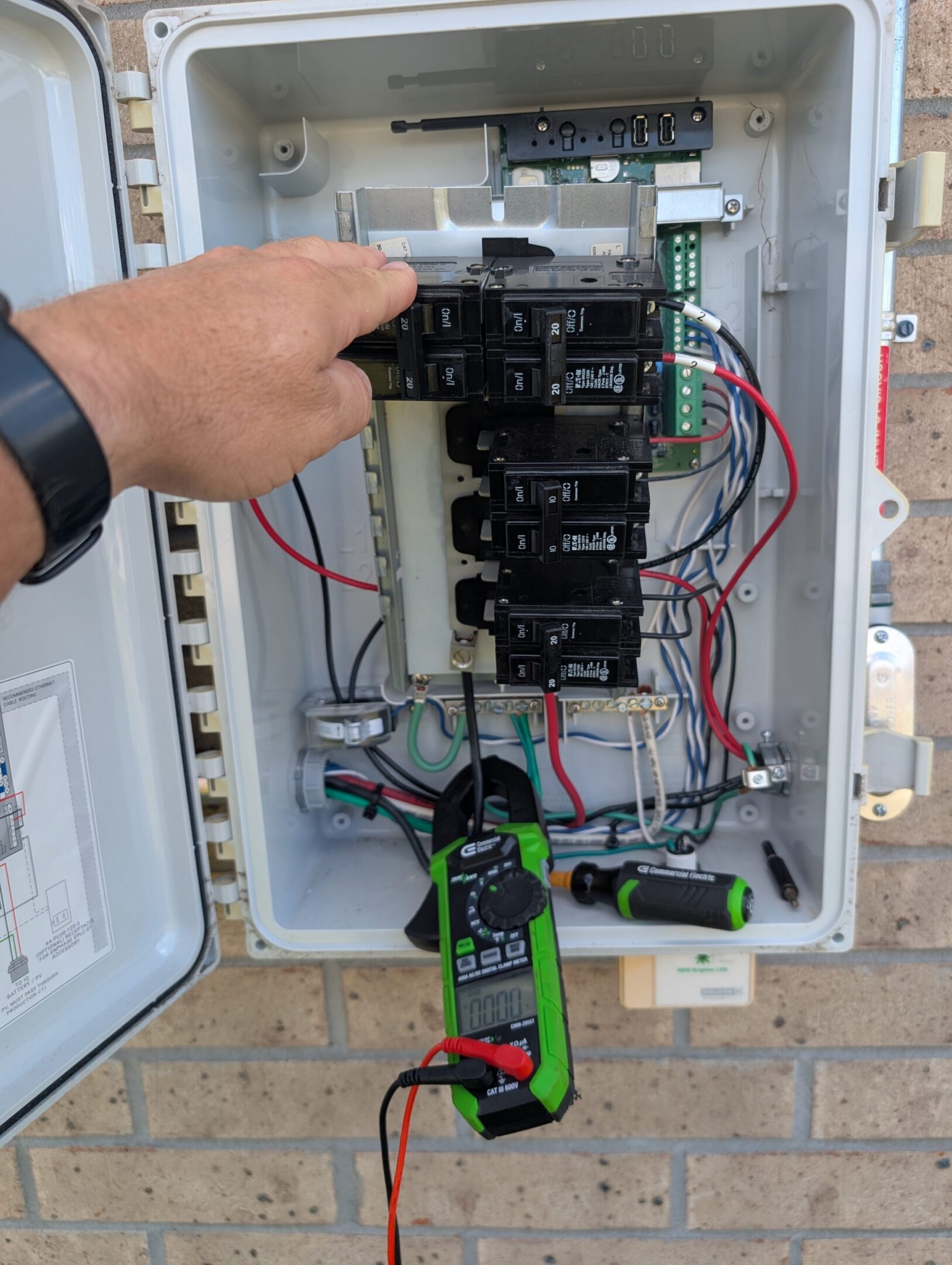 Technician troubleshooting an Enphase solar combiner with a clamp meter.